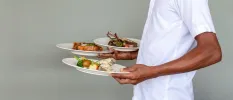 Person in white carrying plates of fish, meat and vegetables designed beautifully
