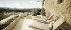 Neutral cushioned loungers next to a stone wall in a sunny terrace, with a view of the surrounding countryside