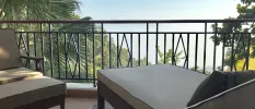 Balcony with black railings, with a cushioned lounger looking over a hillside cloaked in greenery