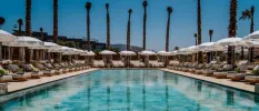 Rectangular swimming pool surrounded by white umbrellas, loungers and palm trees at The View Bouznika 