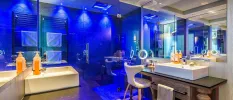 Modern bathroom with a huge shower, blue lighting, twin wooden vanity units and a boucle chair 
