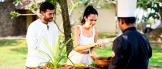 Man and woman in white help a chef prepare food at an outdoor cooking station