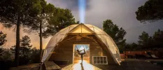 Woman in a yoga pose under a sheer dome surrounded by trees under a dark sky