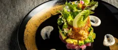 Black plate with a tower of seafood or meat, avocado, salad and edible flowers