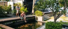 Family dangle their feet over a fish-filled pond among tropical grounds