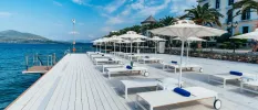 Seafront terrace with white wooden decking, loungers and umbrellas and blue towels under a blue sky
