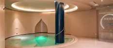 Circular indoor pool with a black pillar support, in a room with a circular ceiling design and LED lighting