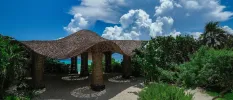 Pergola with wooden stilts and a curved thatched roof, surrounded by tropical greenery and overlooking the sea