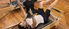 Male in white top and black trousers performing a reformer pilates session