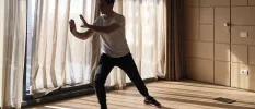 Man in a vest and tracksuit bottoms practices Tai Chi in an airy studio