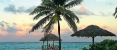 Couple dining under a thatched pergola at the end of a wooden jetty at sunset overlooking the ocean