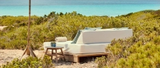 White-cushioned daybed with blue cushions under a parasol surrounded by greenery and with a sea view