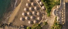 Sandy cove lapped by waves, lined with thatched parasols and loungers