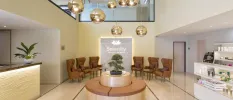 Spa entrance area with a cluster of gold pendant lights, a circular sofa with brown leather and matching armchairs, a large desk and a shelf of cosmetic products