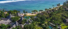 Aerial view of a grey thatched-roof resort, covered in tropical greenery and next to a sandy beach overlooking the ocean