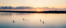 Four people paddle boarding on a lagoon as the sun rises over the jungle in the distance