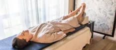 Woman in a beige robe lying on a massage bed with her feet up on a machine