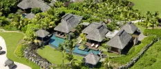 Aerial view of thatched-roof villas, blanketed in palm trees and greenery, with a swimming pool and white loungers visible on one deck
