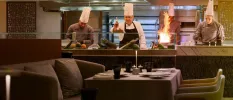 Chefs hard at work at a live cooking station as seen from the restaurant dressed in neutral colours