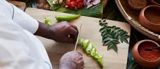 Chef in whites chopping up vegetables on a wooden chopping board surrounded by pots of spices