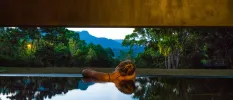 Woman relaxing a swimming pool with her head on her shoulder as she looks out at mountains and forest
