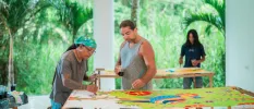 Three people painting colourful murals in an open-air art studio surrounded by tropical vegetation