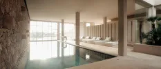 Indoor swimming pool next to a stone wall with white loungers opposite