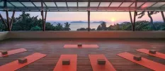 An open-air pavilion with an ocean view set up for a class with red and brown yoga mats and blocks
