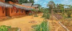 Low-rise orange building with a thatched roof, next to a kitchen garden under a blue sky