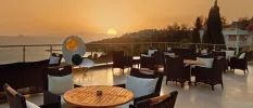 Rooftop sea-facing terrace at sunset, with black rattan chairs and wooden tables, and a giant oyster sculpture with a black pearl and the word 'Sianji' written in gold