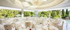 Elegant open-sided restaurant with a domed ceiling, glittering chandelier, white chintzy tablecloths and surrounding gardens