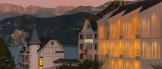 Chenot Palace at night, all white buildings and towers with grey turrets, with Swiss flags on the entrance and Lake Lucerne and the Alps in the background