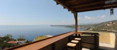 Thatched-roof open-sided terrace with wooden stalls and a sweeping Aegean Sea view