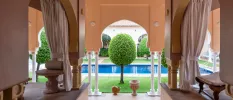 Relaxing area with terracotta walls and white curtains overlooking a swimming pool surrounded by trees