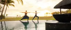 A man and woman with knees bent and arms outstretched next to a water feature overlooking the ocean