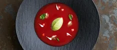 Dark grey bowl with a red think liquid inside, garnished with green leaf-like vegetables