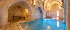 Indoor pool in a warmly lit vaulted room with a stone floor, stone walls and a stone ceiling