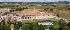Terracotta-roofed, sand-coloured monastery with a swimming pool, surrounded by greenery and vineyards