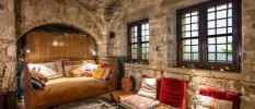 Cosy, patterned low-level chairs and cushions in a room with stone walls and a stone ceiling and dark-wood windows