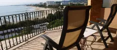 Black wrought-iron balcony with two chairs and a small table overlooking the sea and a golden beach