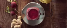 Jar of bright pink liquid surrounded by radishes, ginger and an apple
