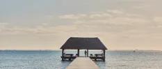 Figure standing in an open-air pavilion at the end of a wooden jetty, suspended above the Caribbean Sea