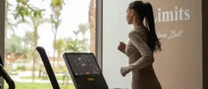Woman in active wear running on a treadmill in front of a window overlooking tropical gardens