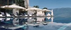 Infinity pool lined with ivory cushioned loungers and parasols, with mountain peaks in the background
