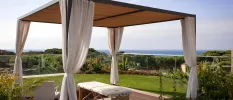 Outdoor treatment bed under a four-poster cabana, surrounded by a garden and with a sea view