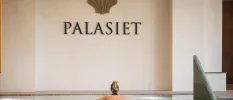 Woman swims in an indoor pool under a cream wall reading 'PALASIET'