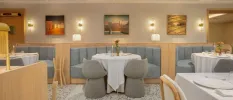 Modern restaurant with grey booth seating and chairs, a pebble-design floor, crisp white tablecloths and soft wall lighting with framed abstract pictures