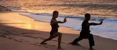 Two figures at sunset on the sand practicing yoga as waves wash ashore