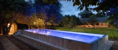 Rectangular swimming pool lit by surrounding lights as the sky darkens 