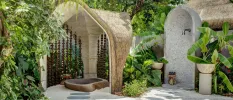 Cobbled stone courtyard with thatched-roof cubbyholes, with an outdoor shower and bathing area fringed with tropical greenery